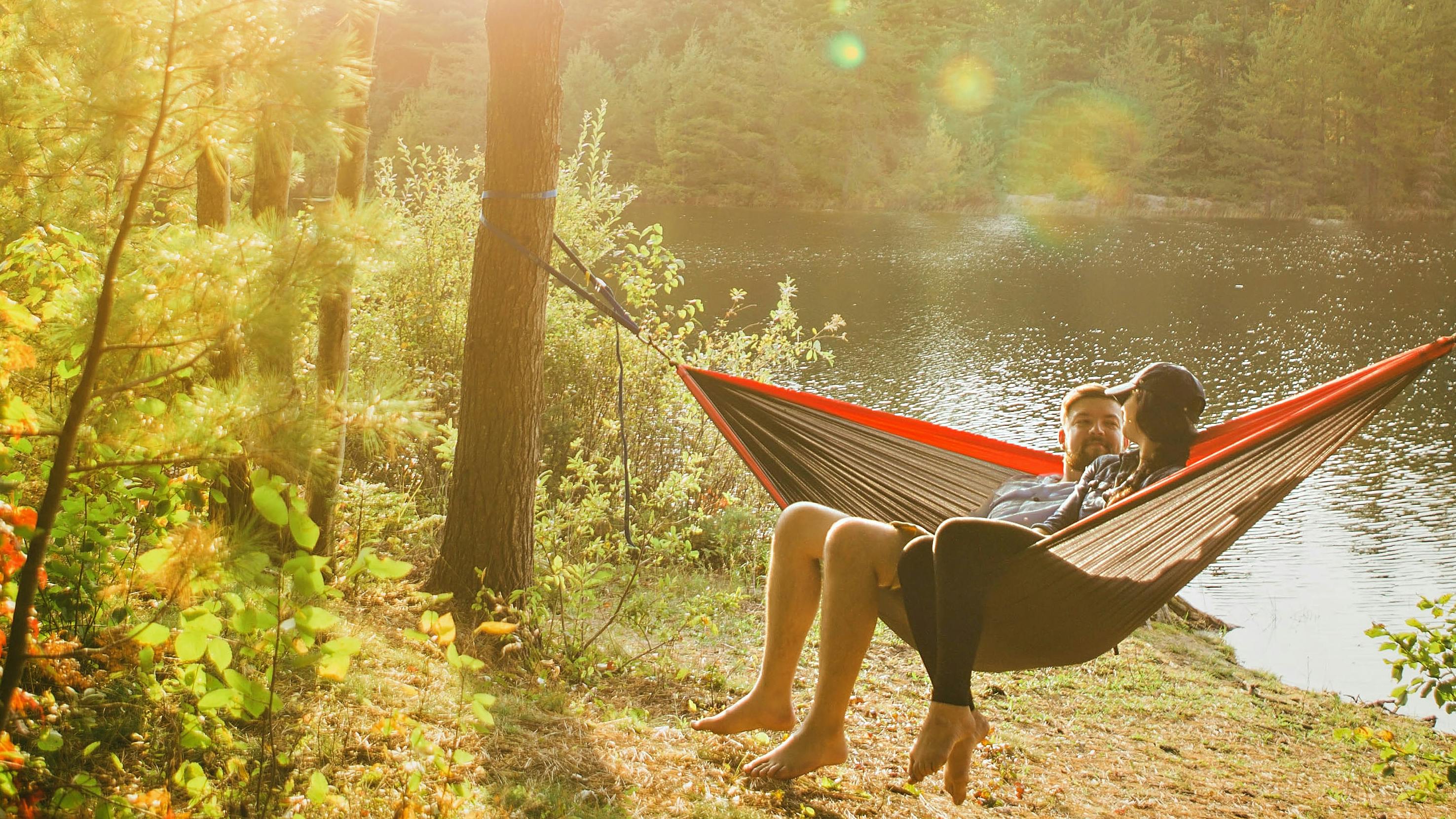 Two people sit in a hammock by a lake