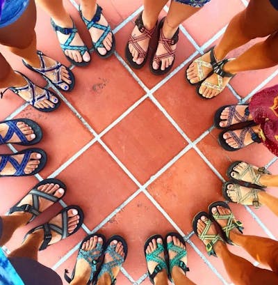 Twelve pairs of feet all wearing the same style of sandal.