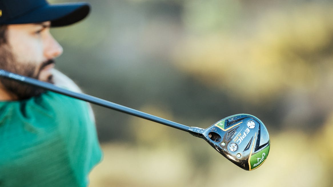 The Callaway fairway wood is in focus and the man swinging it back is blurry in the background.