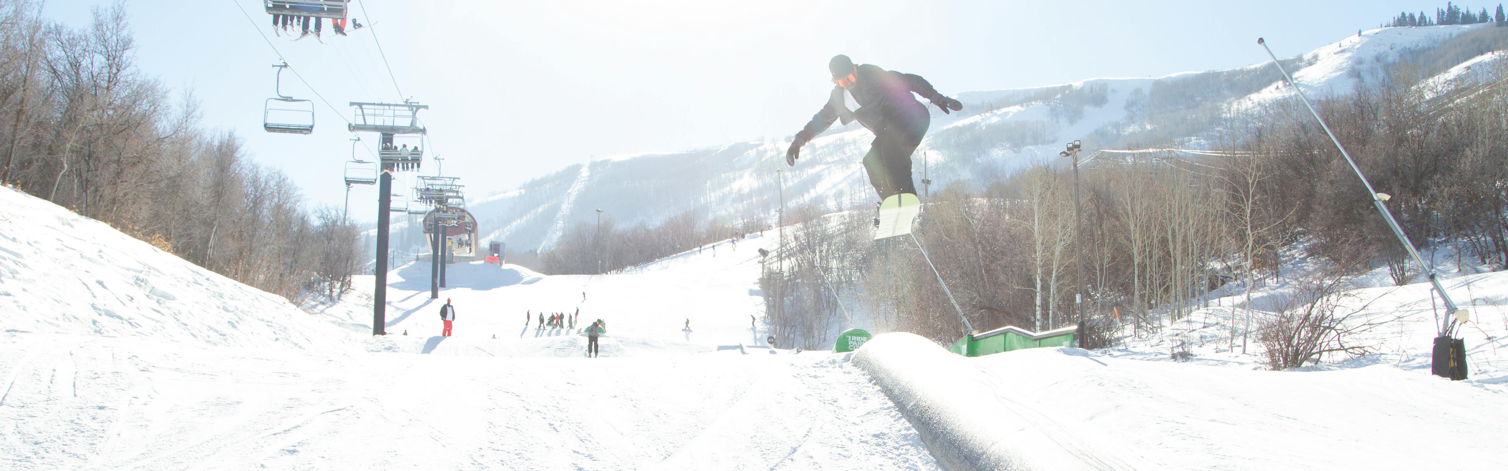 A snowboarder jumps above a rail. 