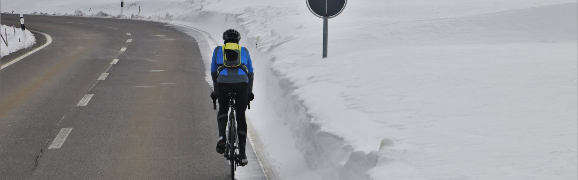 A cyclist pedals up a hill. It is snowy.