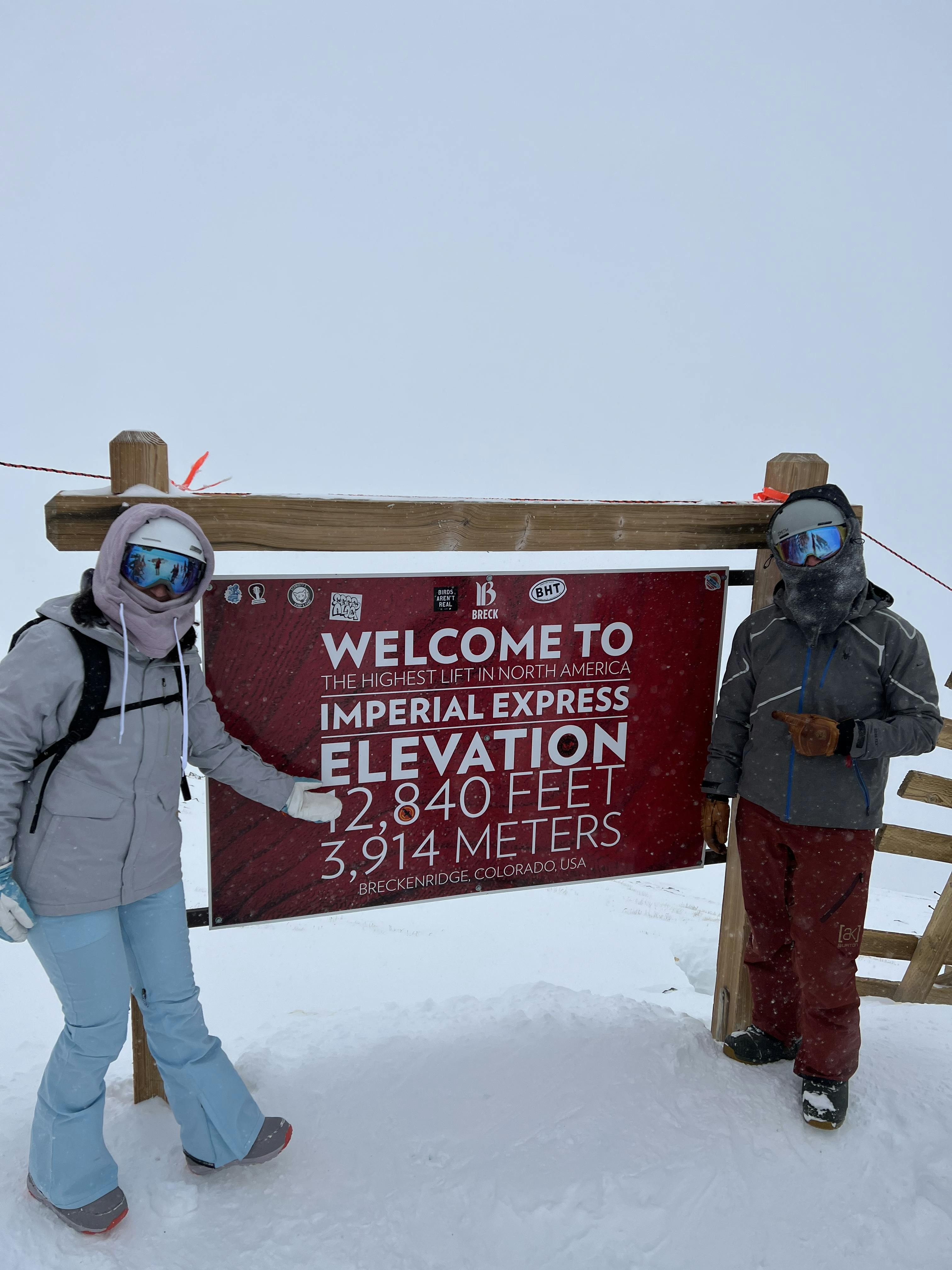 Two snowboarders standing in front of a sign. 