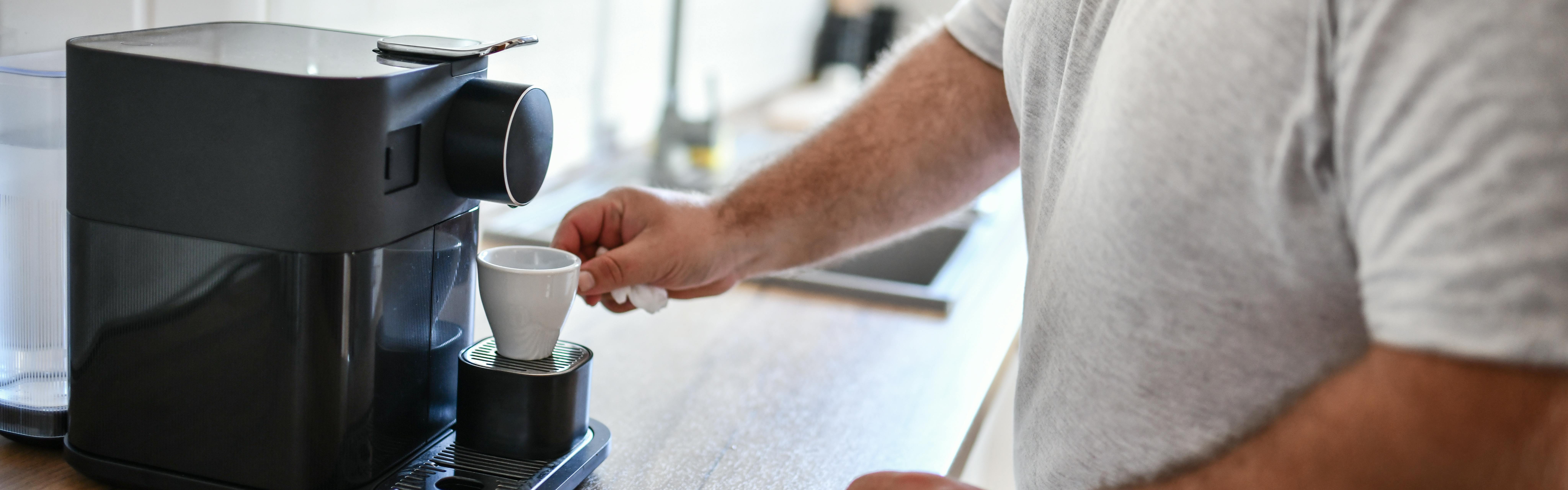 A man reaches out to pick up a ceramic espresso mug from his espresso machine.