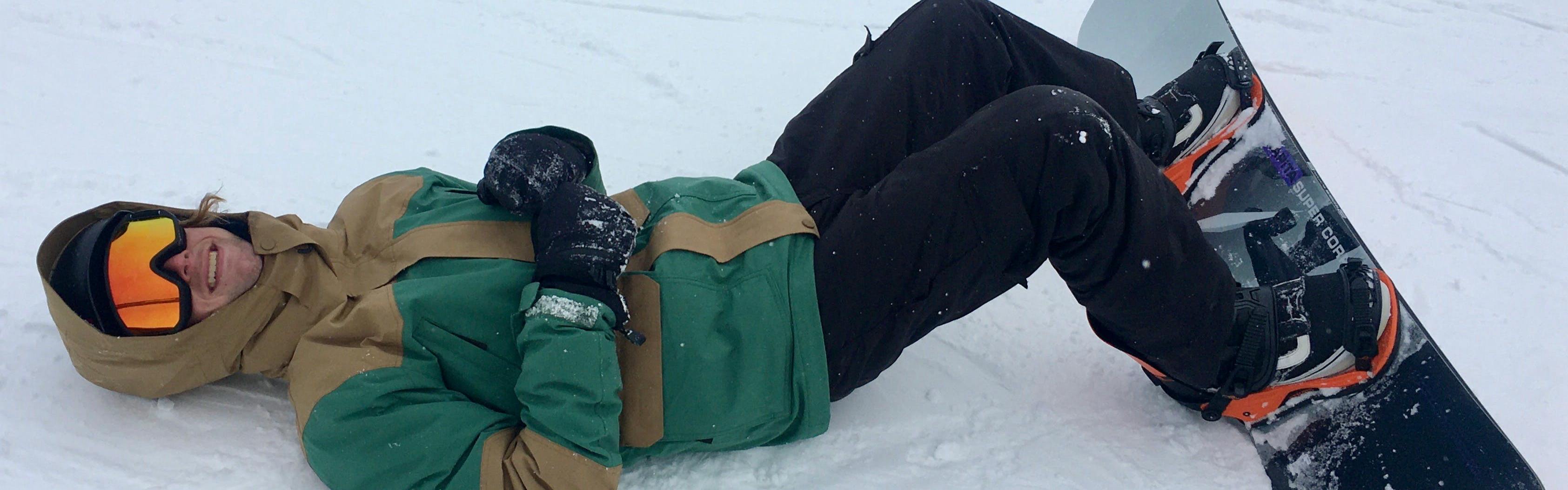 A snowboarder lying on the snow with the CAPiTA The Outsiders Snowboard · 2023 on. 