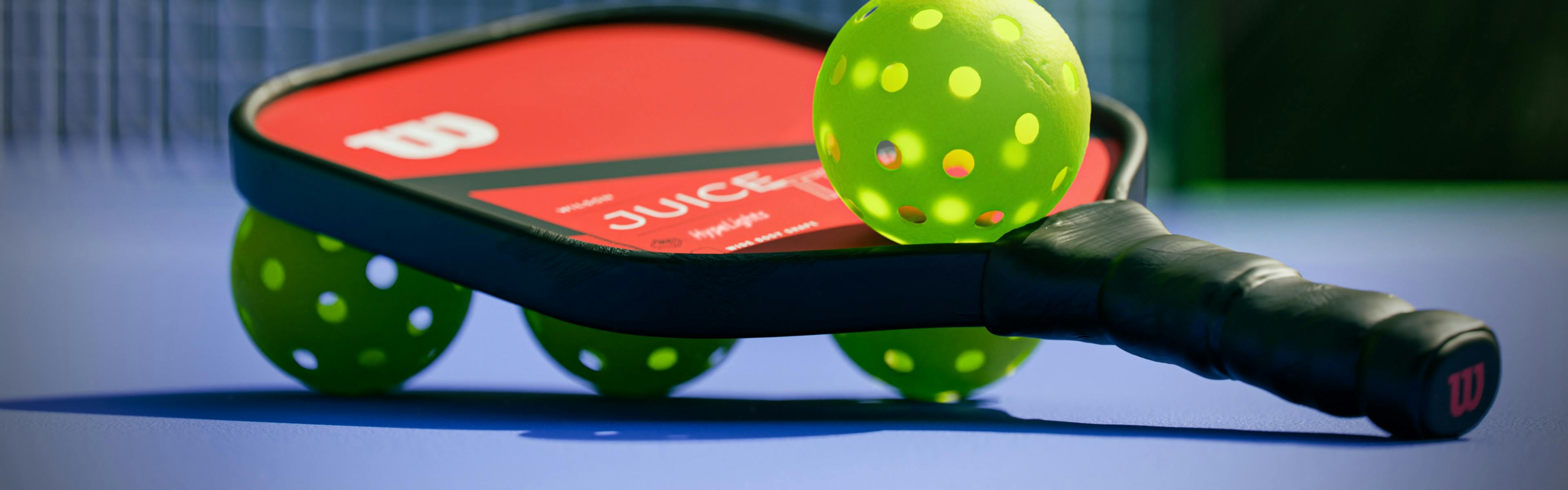 A pickleball paddle with four pickleballs on it. 