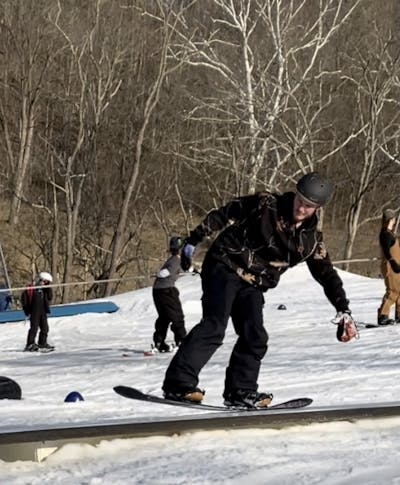 A snowboarder riding a box in a terrain park with the DC Control Snowboard boots on. 