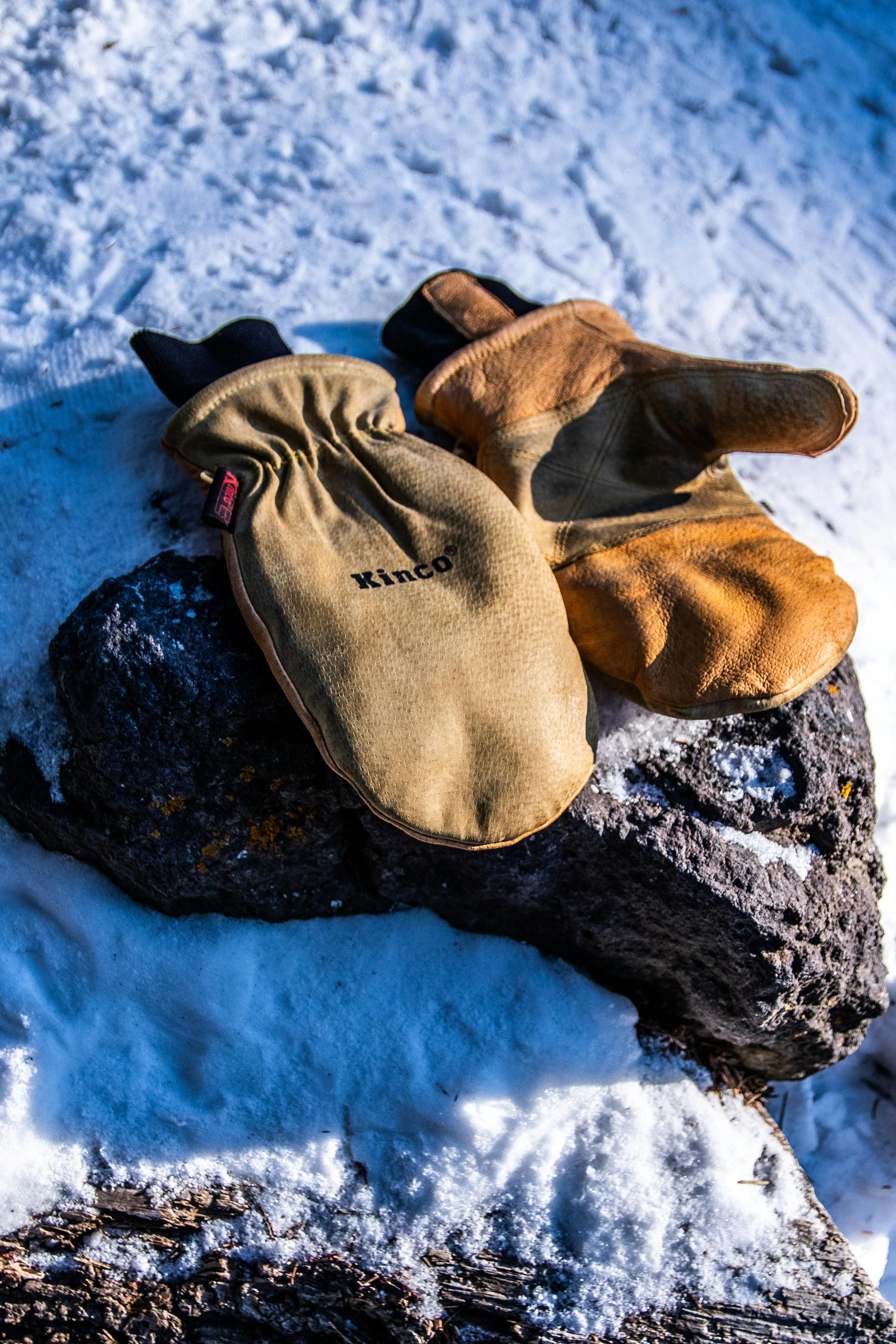 A pair of mittens sit on a rock in the snow.