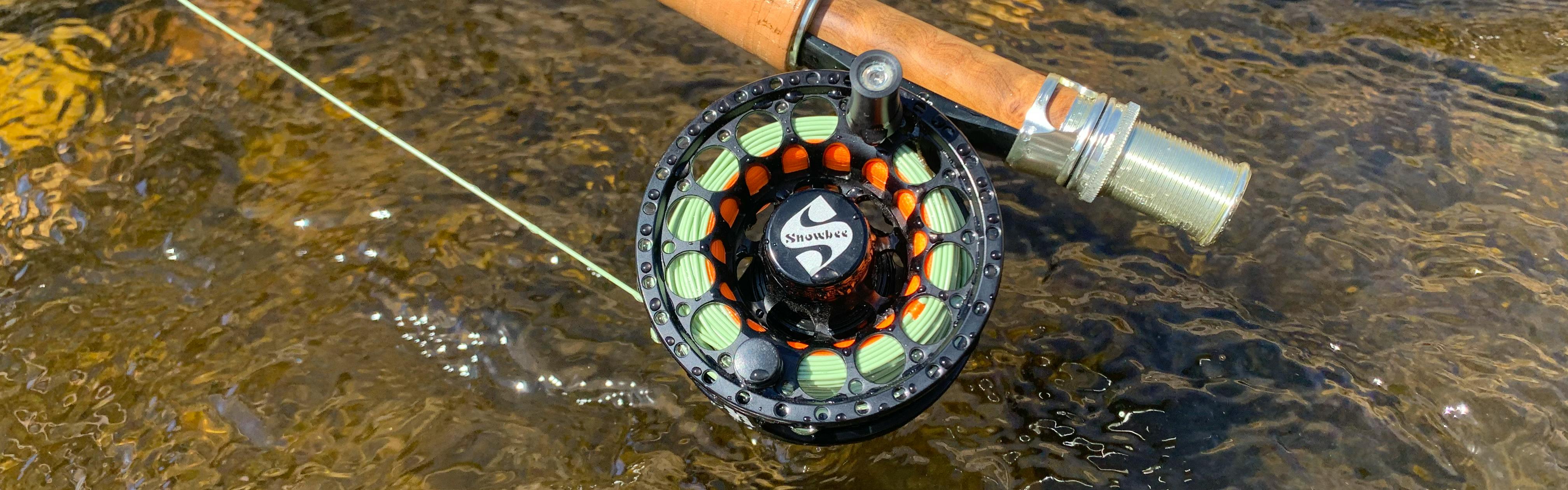An image of a Snowbee flyfishing reel sitting above a water source.