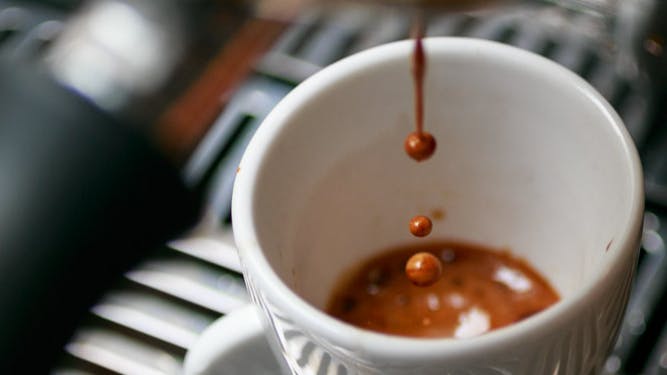 Espresso drips from the machine into a white cup.