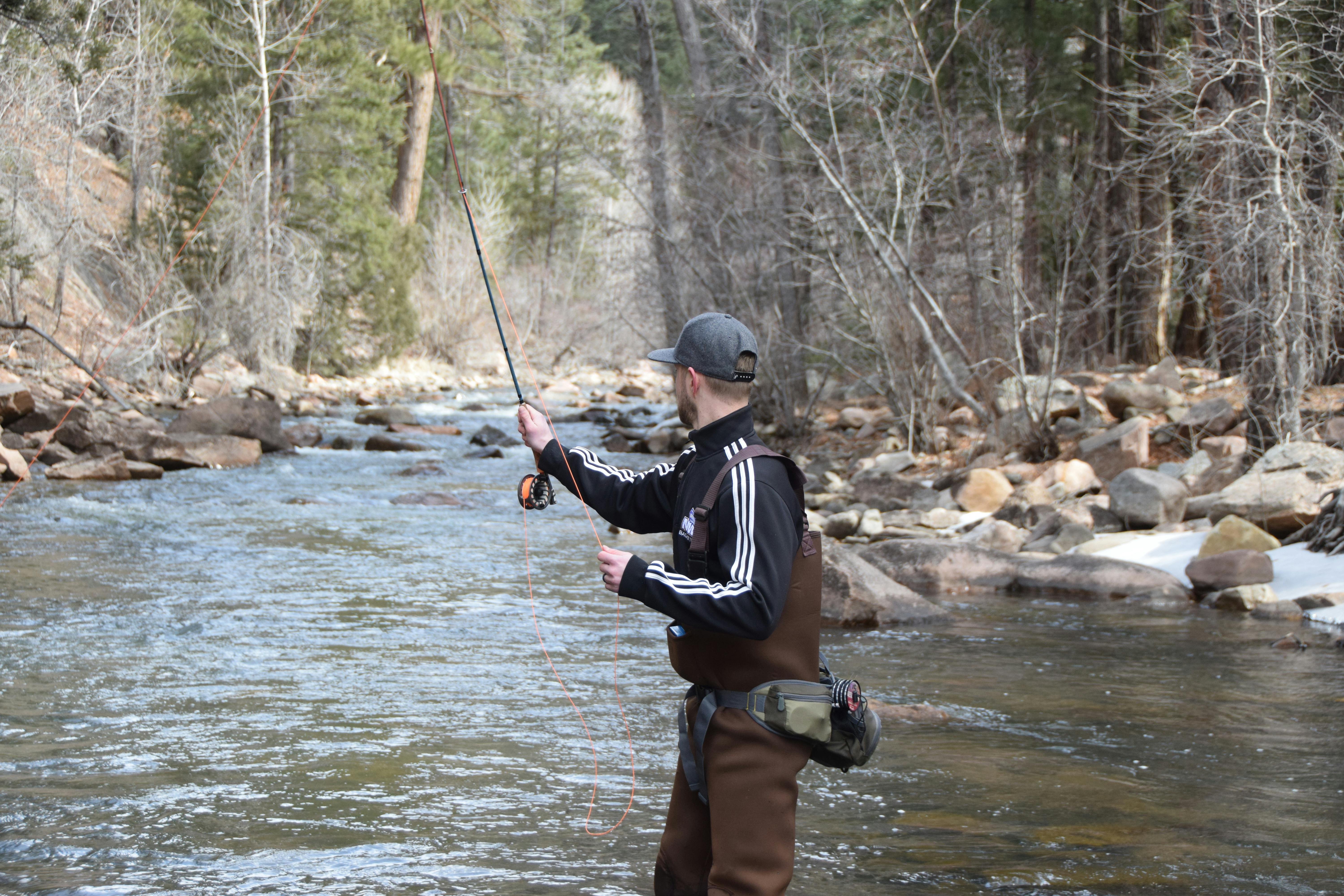 A man in waders fly fishes in a river.