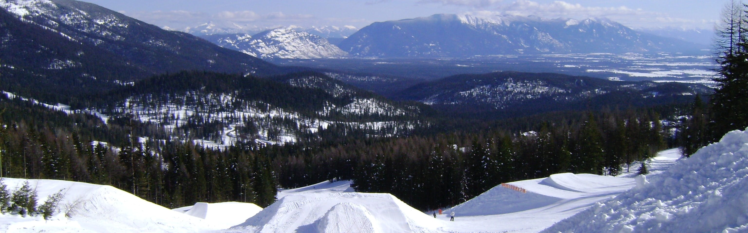 Ski jumps with trees and more mountains in the distancw