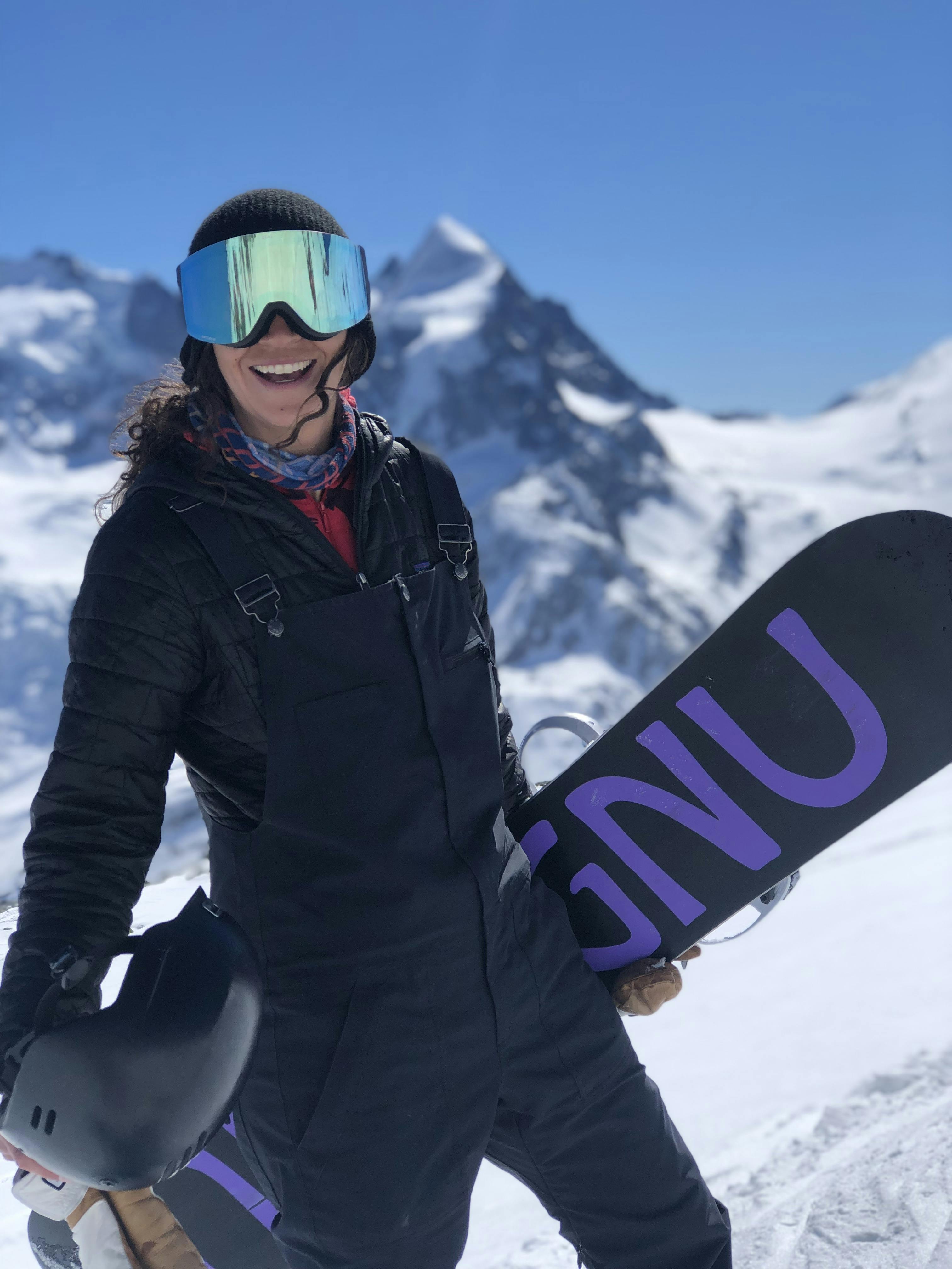 A snowboarder holding her snowboard and wearing the Zeal Optics Beacon Goggles · 2021. 