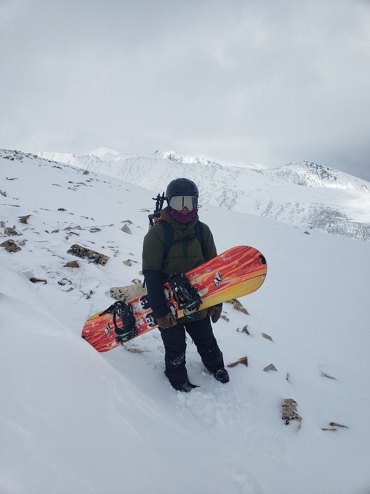 A woman stands and holds her snowboard in front of her. The landscape and sky are full of snow.
