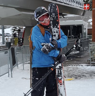 A skier standing in front of a lift holding a pair of skis. 
