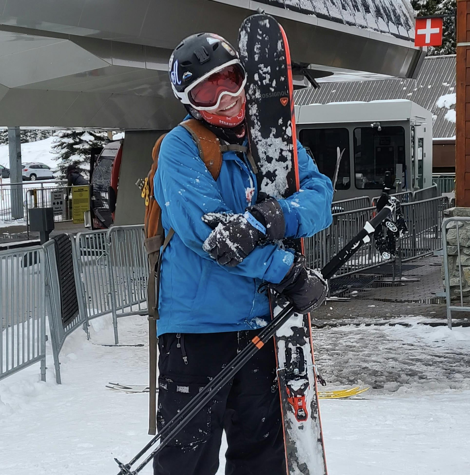 A skier standing in front of a lift holding a pair of skis. 
