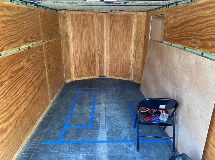 The inside of a cargo trailer. There is wood on the walls and tape on the floor.