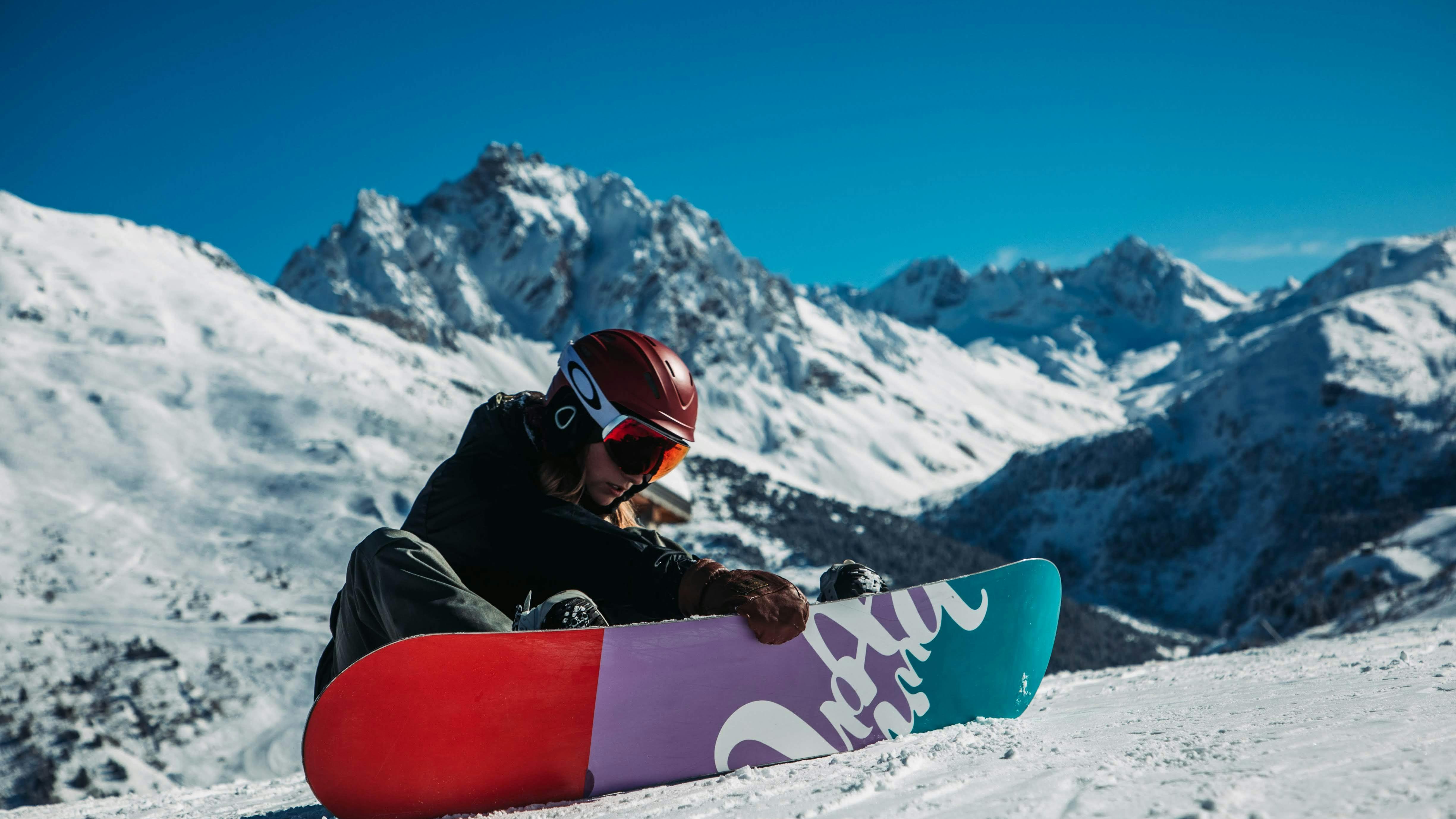 A snowboarder sits in the snow with their board in front of them