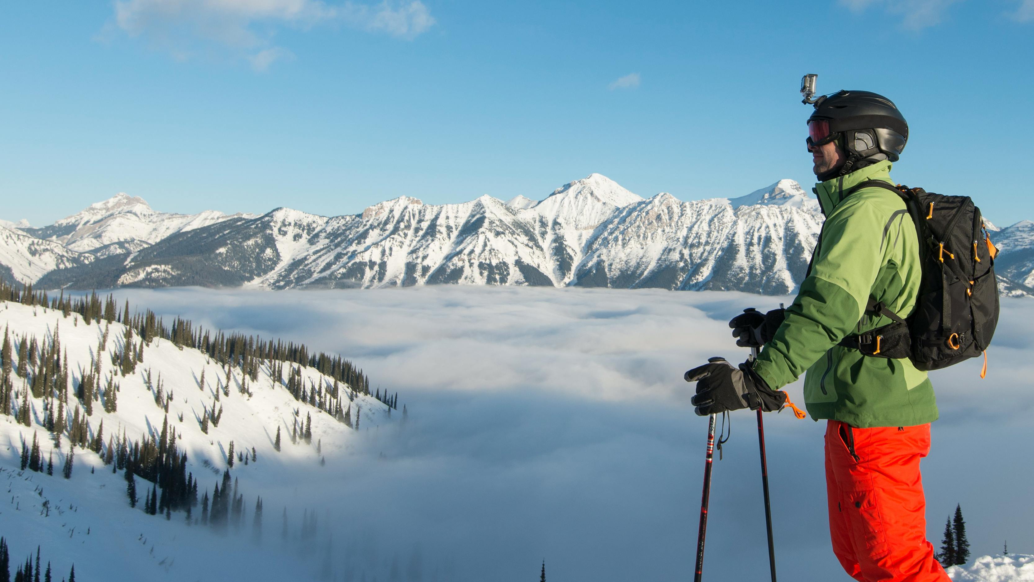 A skier stands on a ridge and looks out towards mountains in the distance. 