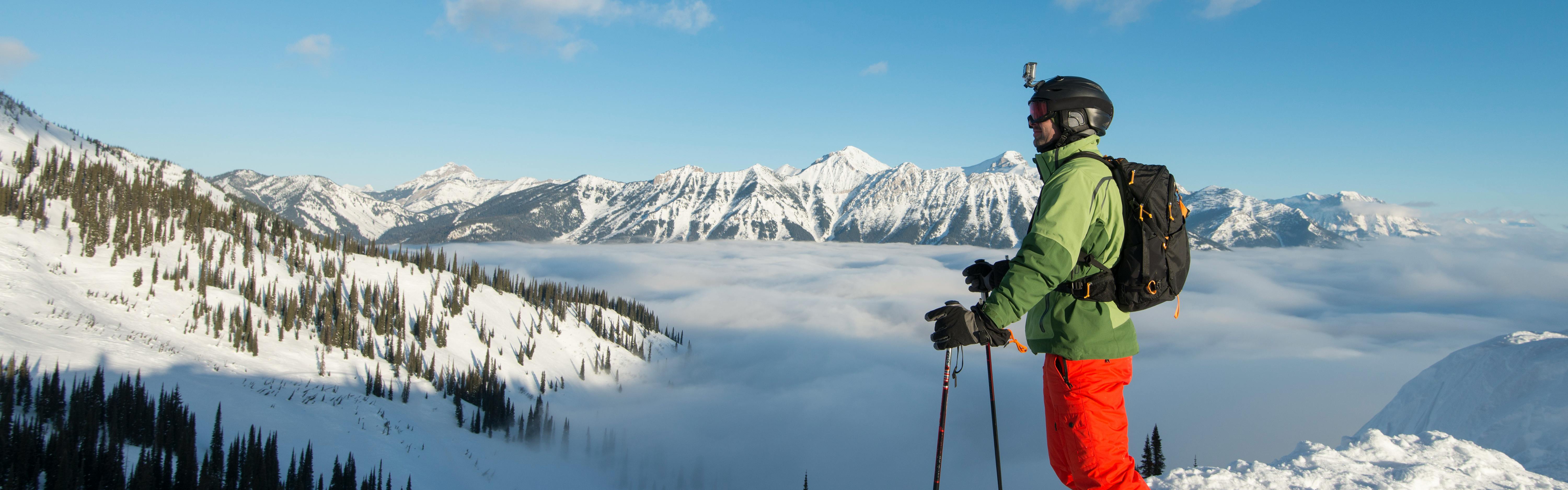 A skier stands on a ridge and looks out towards mountains in the distance. 