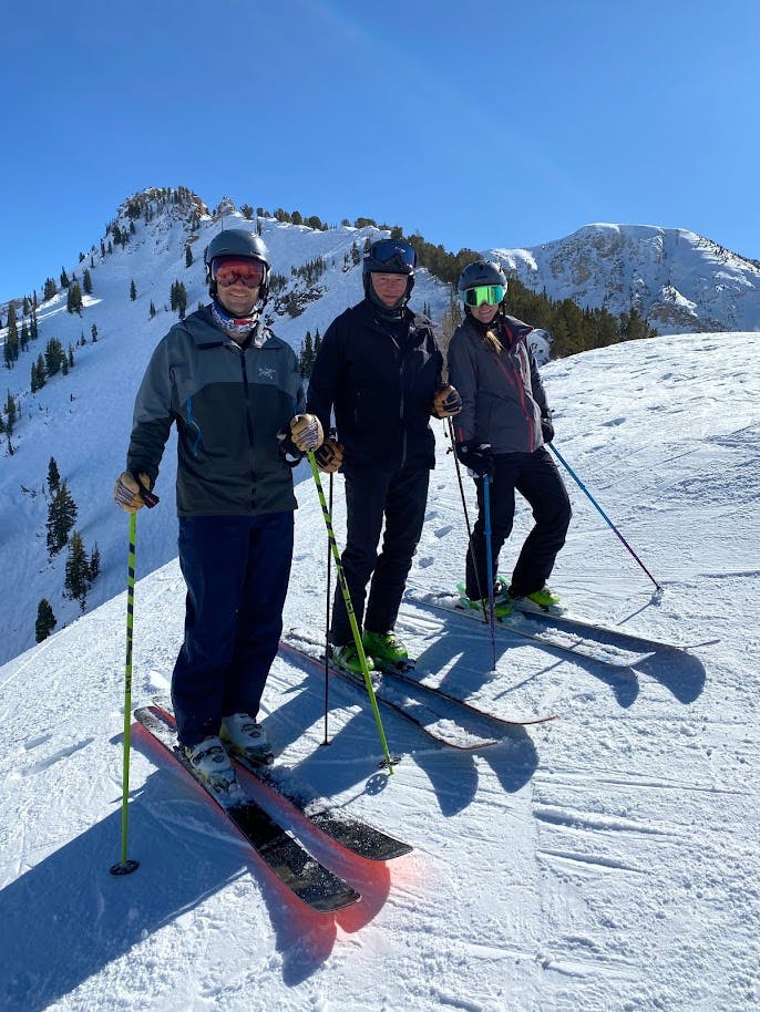 Three skiers standing at the top of a snowy mountain. 