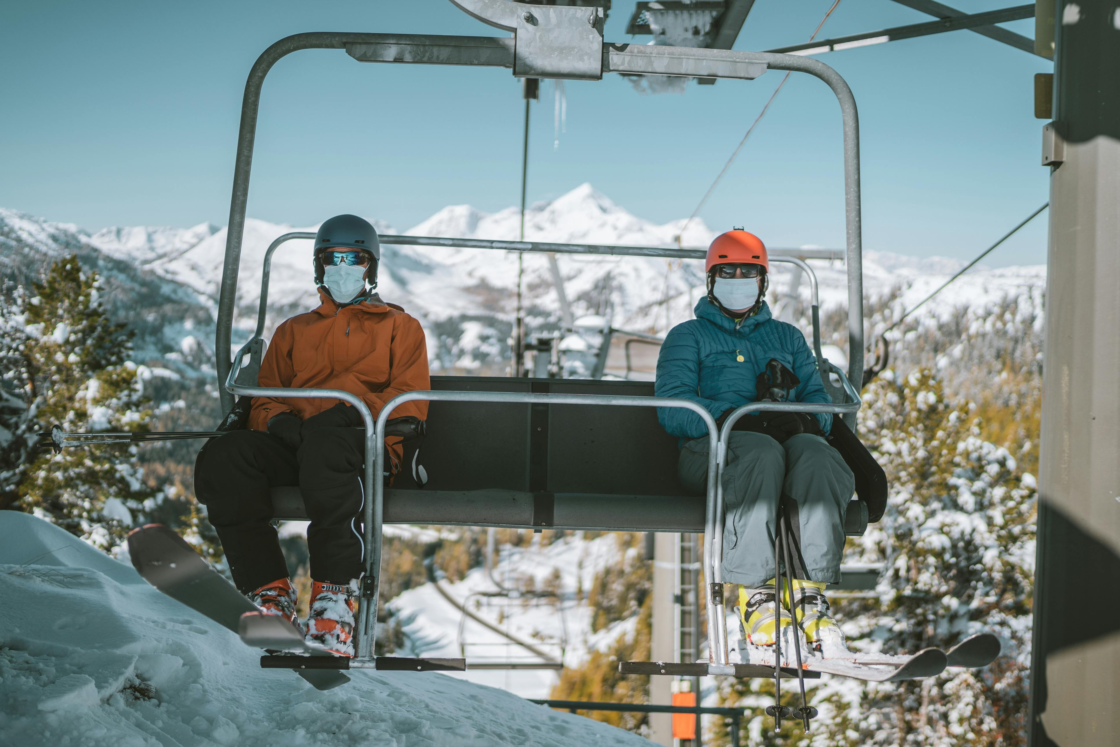 Two people in masks ride a chairlift