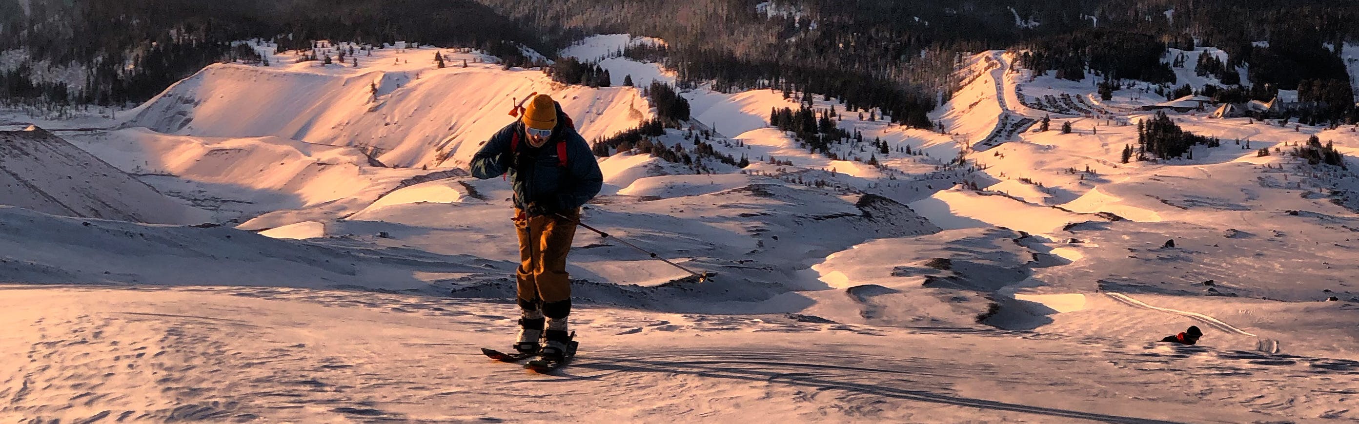 A snowboarder walking up a hill at sunrise.