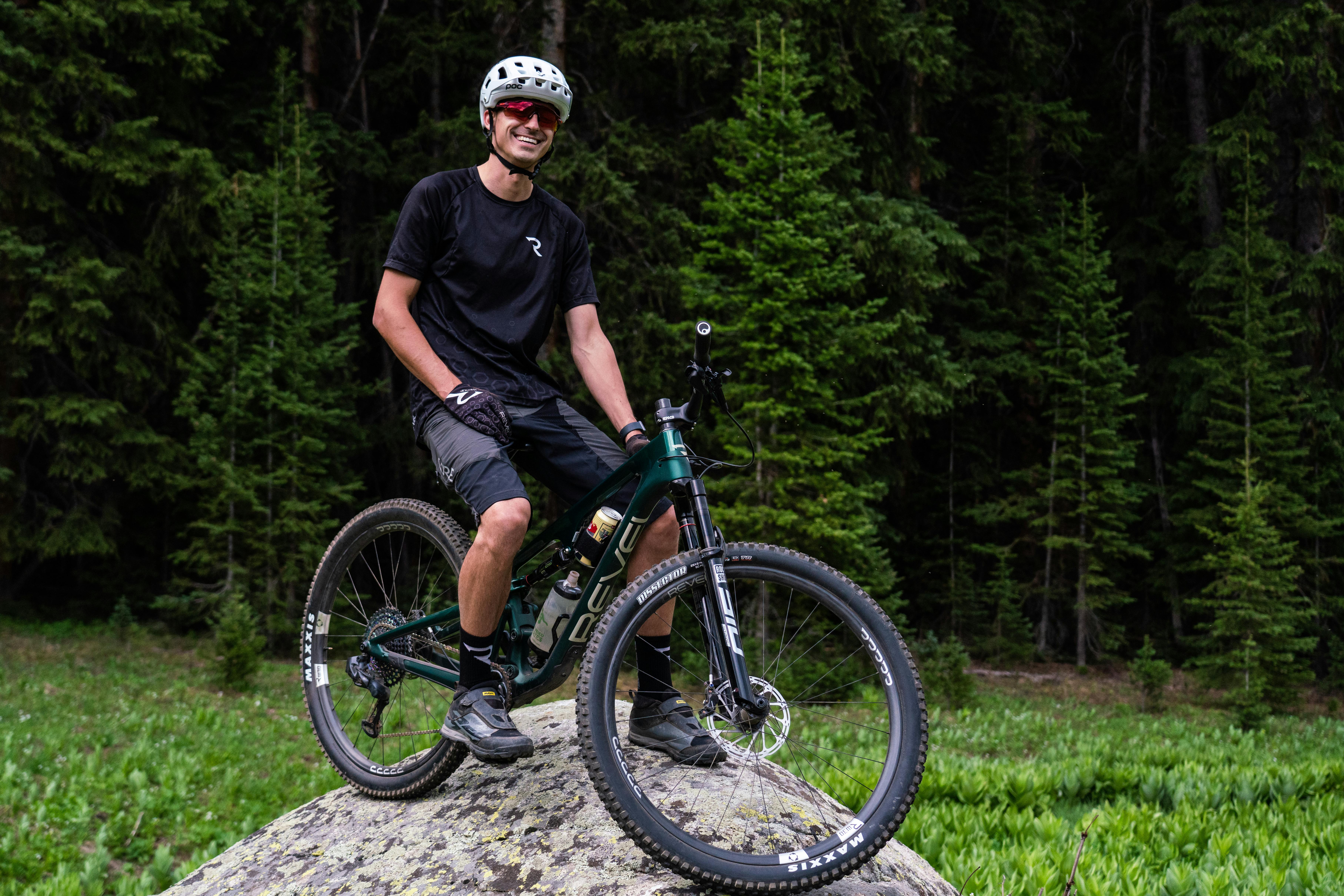 Revel Bikes Founder Adam Miller sitting on his mountain bike on a rock with a forest in the background.