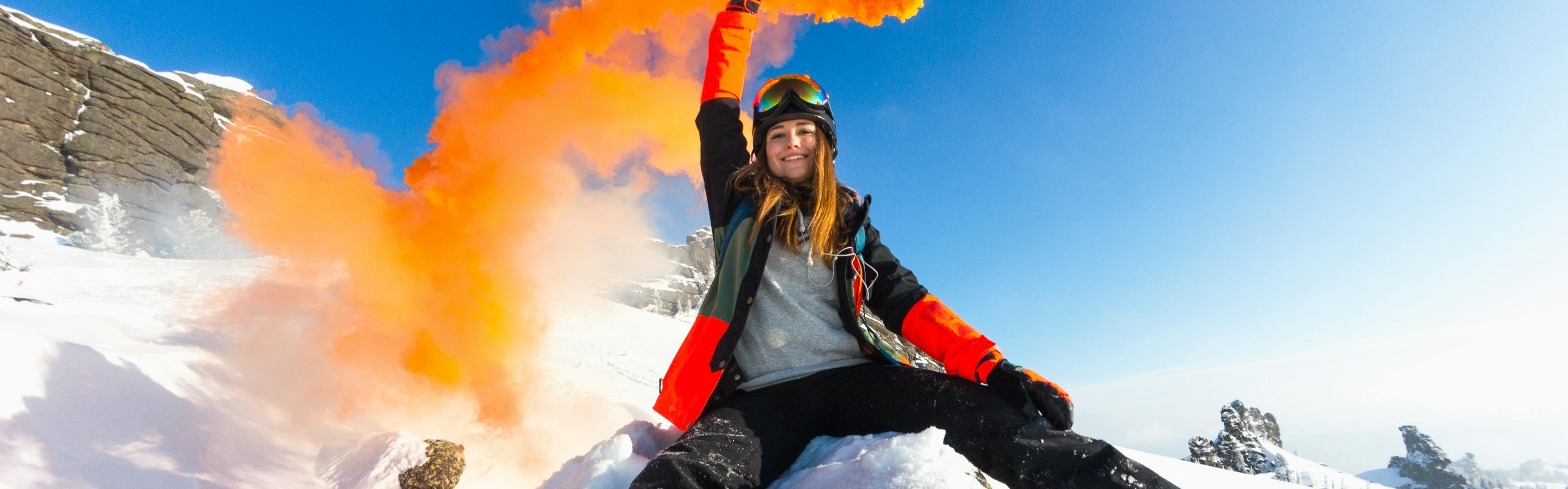 A woman in ski gear sits on a snowy rock with a firework.