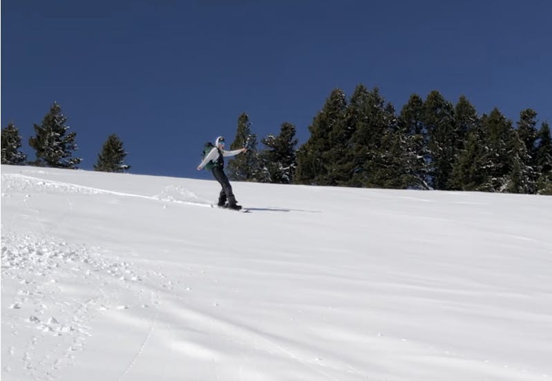 A splitboarder riding down a snowy trail. 