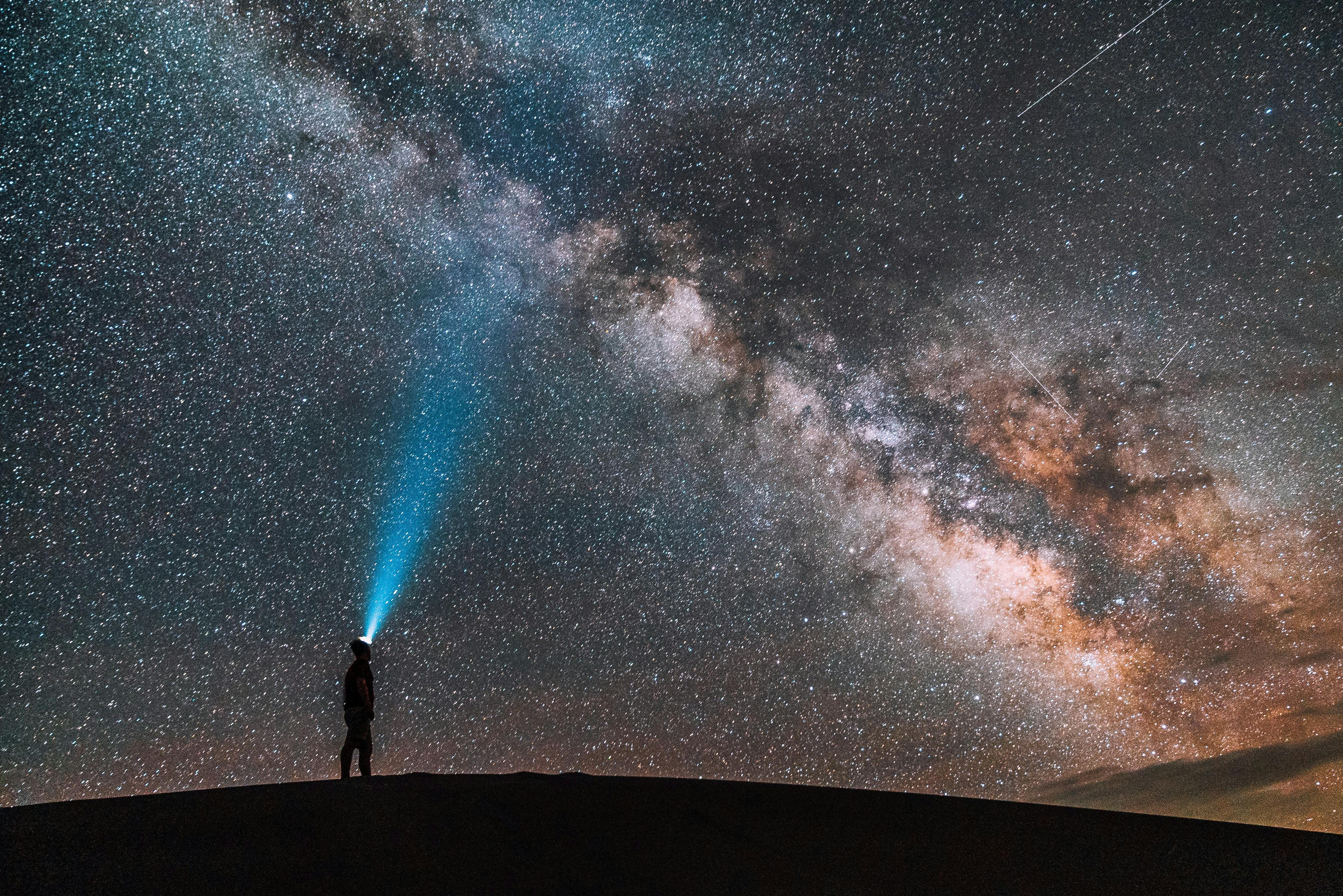 Someone stands on a ridgeline and shines a beam into the night sky. The Milky Way shines bright and the sky is crowded with stars. 