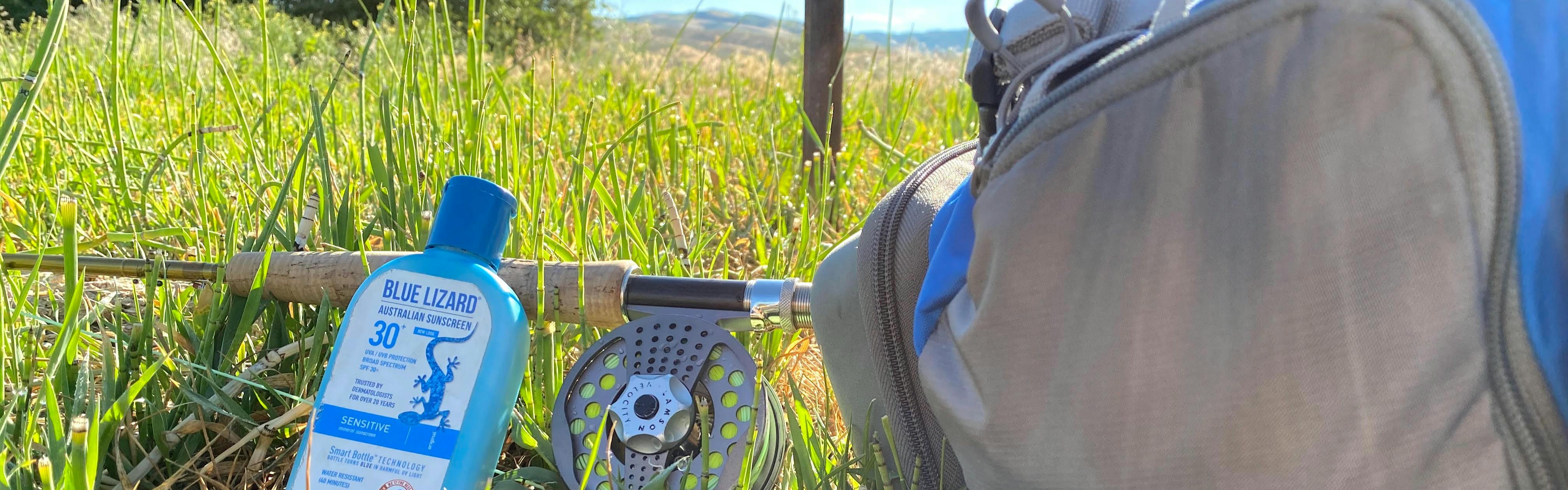 A fly fishing pack, sunscreen, and rod and reel laying in the grass