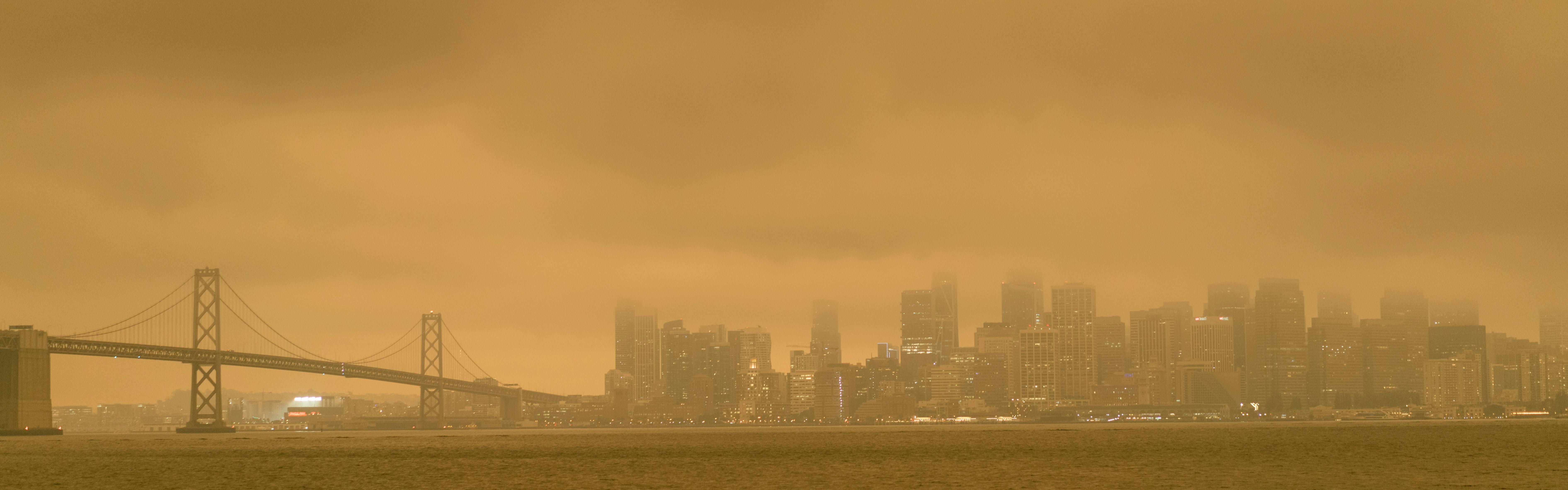 A city with orange and grey smoke engulfing the buildings. 