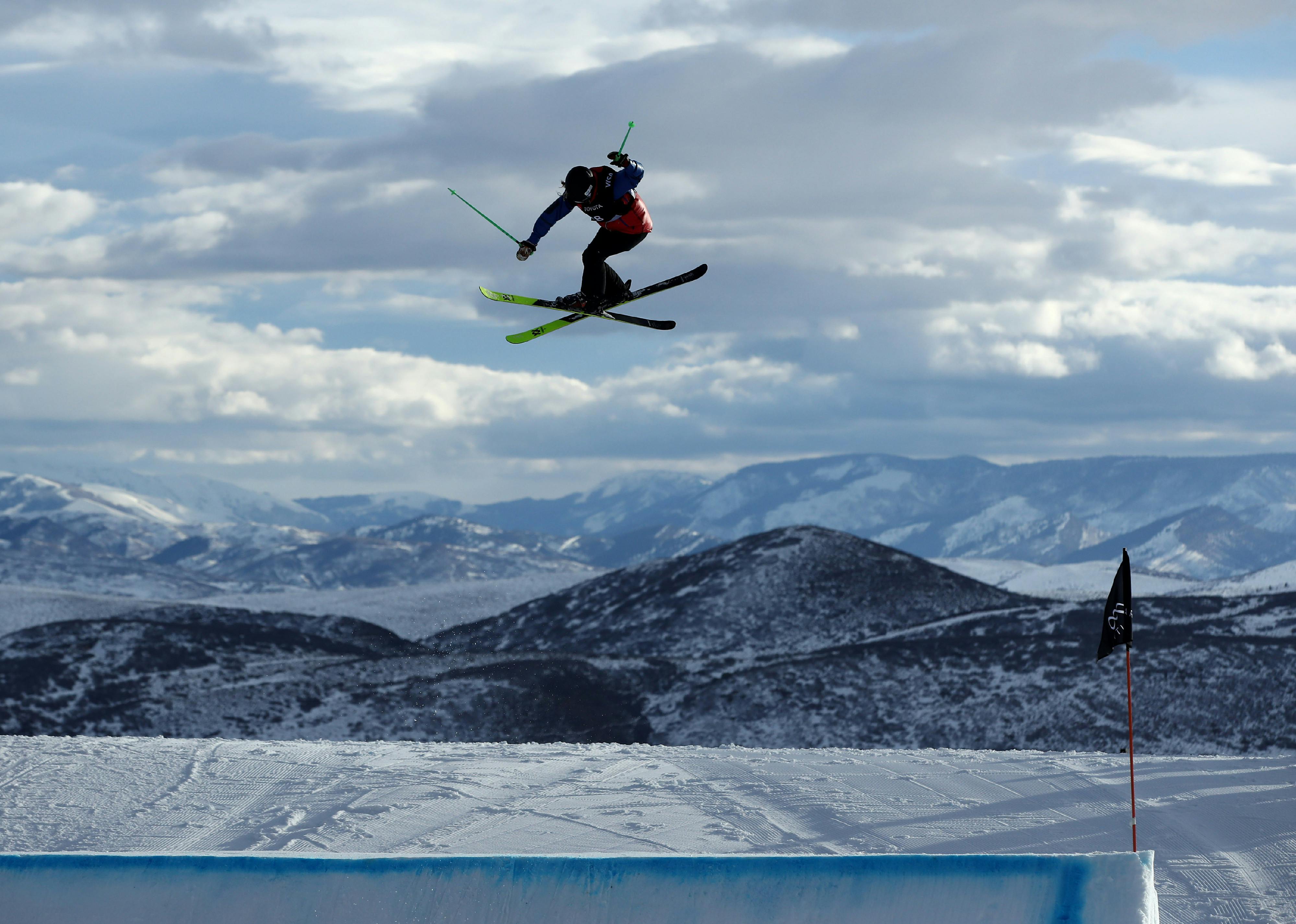 A skier flying through the air executing a jump with mountains in the background