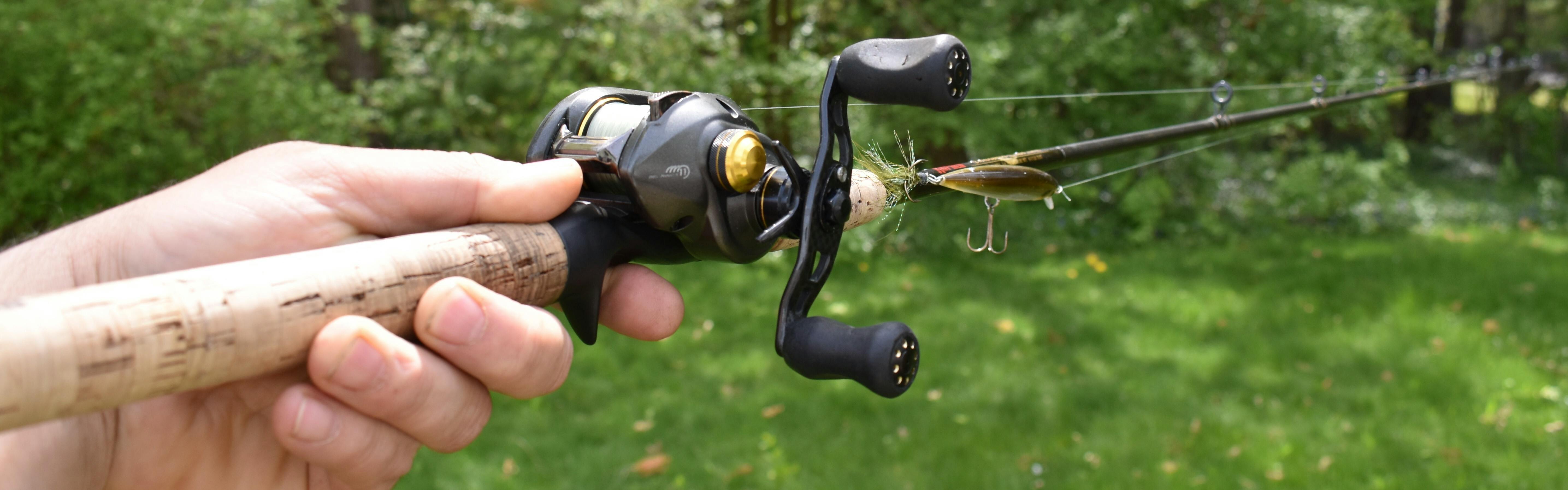 The author holds out a baitcasting reel over a lush lawn.