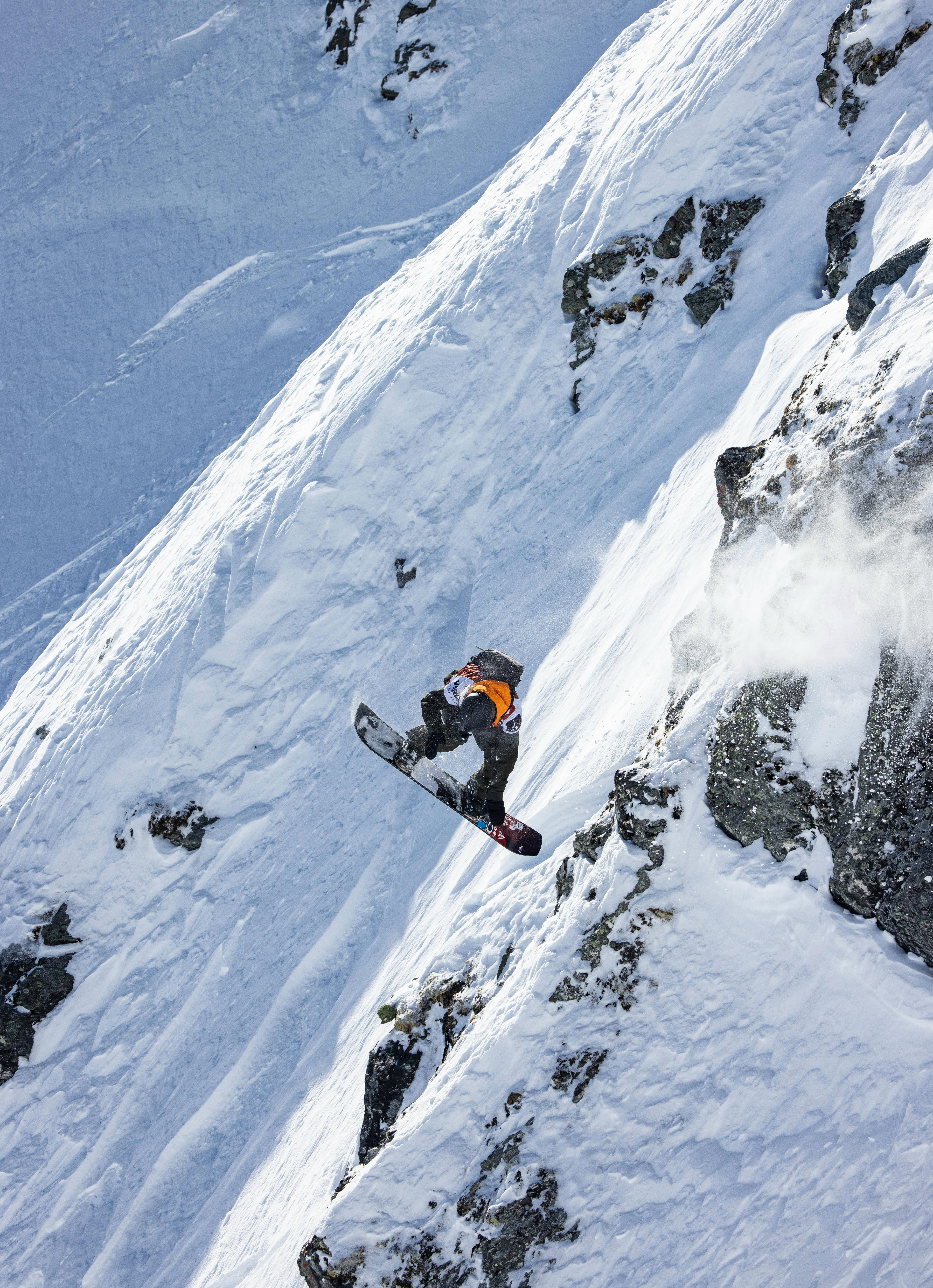 A snowboarder catches air and grabs the bottom of their board when riding in Verbier. 