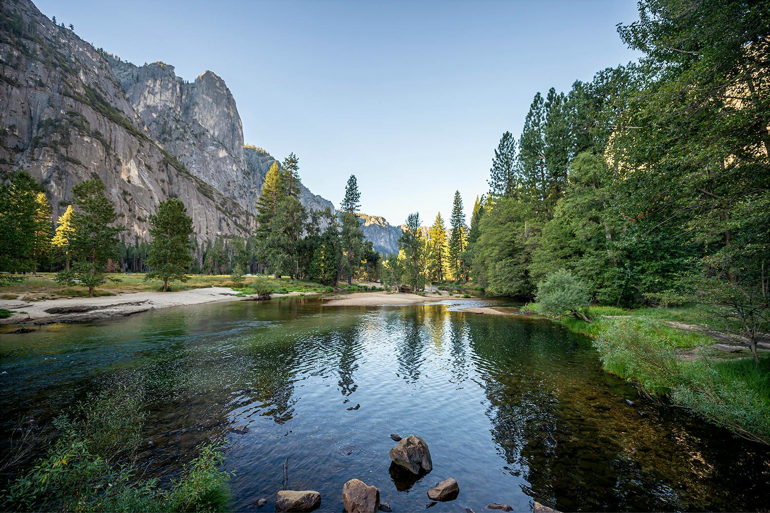 A peaceful shallow lake tucked amongst trees and a towering granite cliff in Yosemite National Park