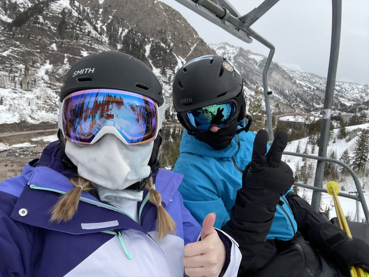 Two skiers sitting on a chairlift with helmets and goggles.