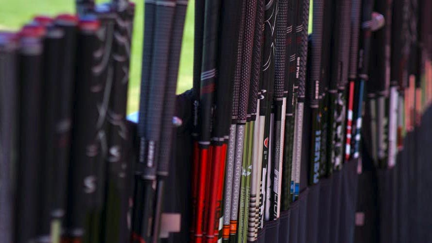 Golf clubs are lined up standing in a row on a golf course. 