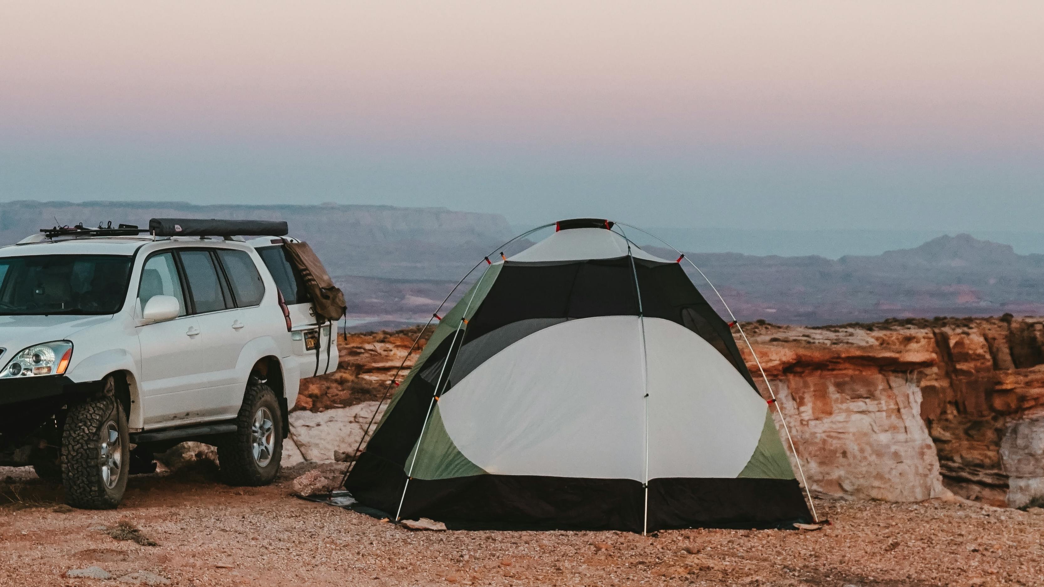 Tent next to a car. Canyons and mountains are in the background.