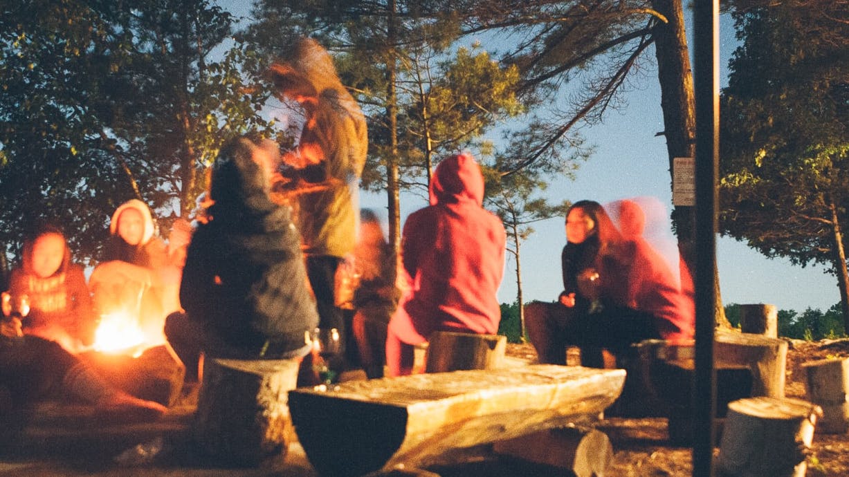 Friends circle around a campfire at night.