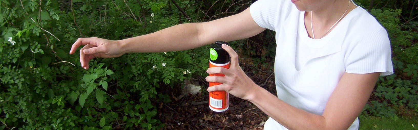 A woman spraying her arm with insect repellant. 
