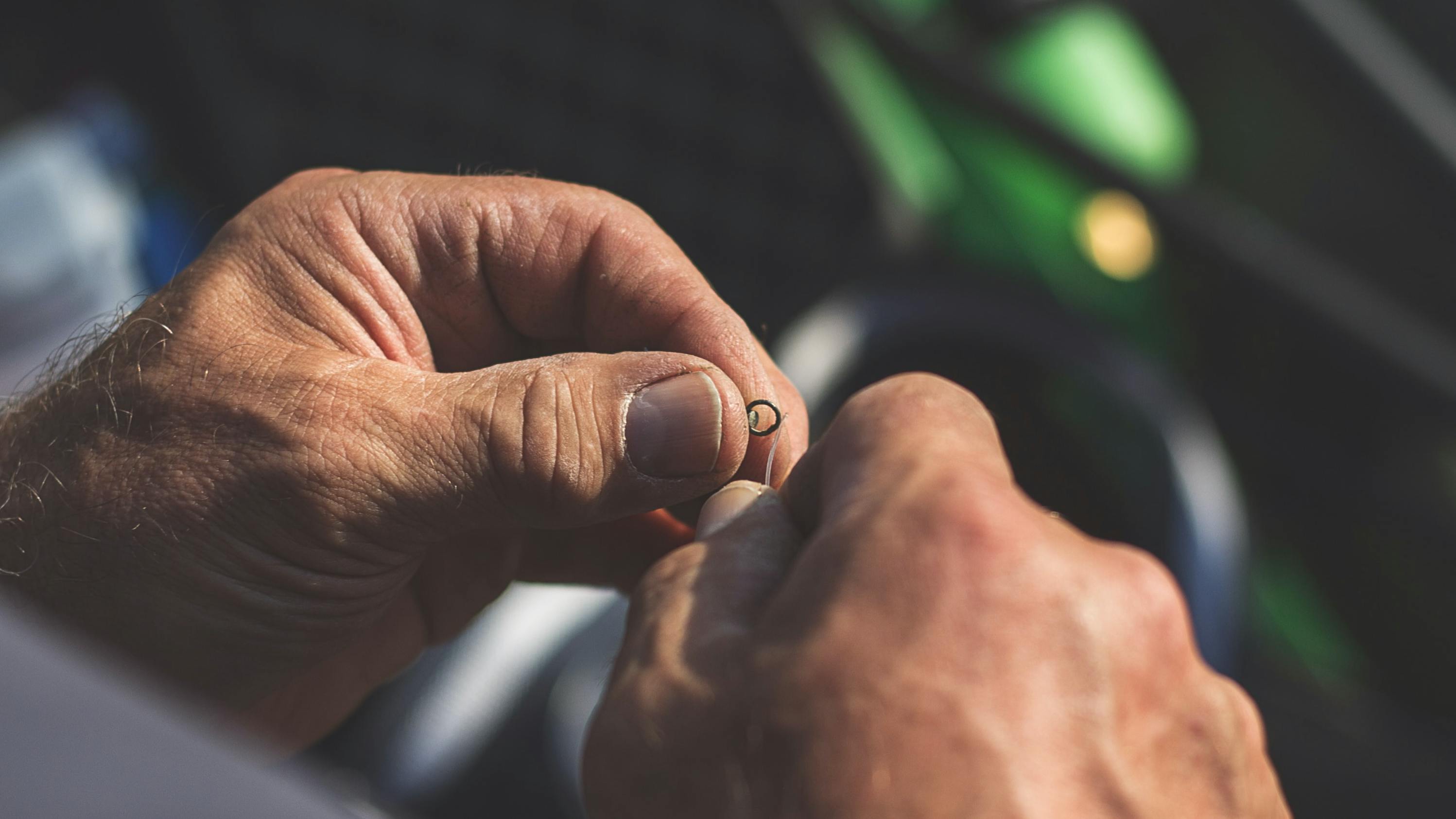 Close up of a mans hands tying a fly to a fishing line.