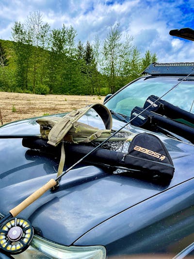 A fly fishing setup lays on top of the hood of a car.