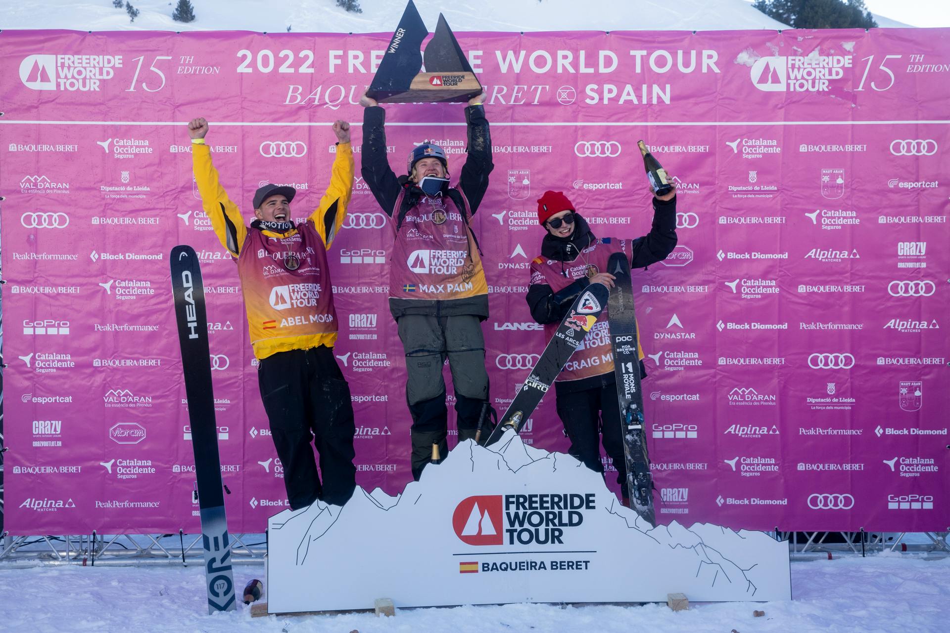 The three male skiers who came in on top stand on the podium with their skis and hold up trophies. 