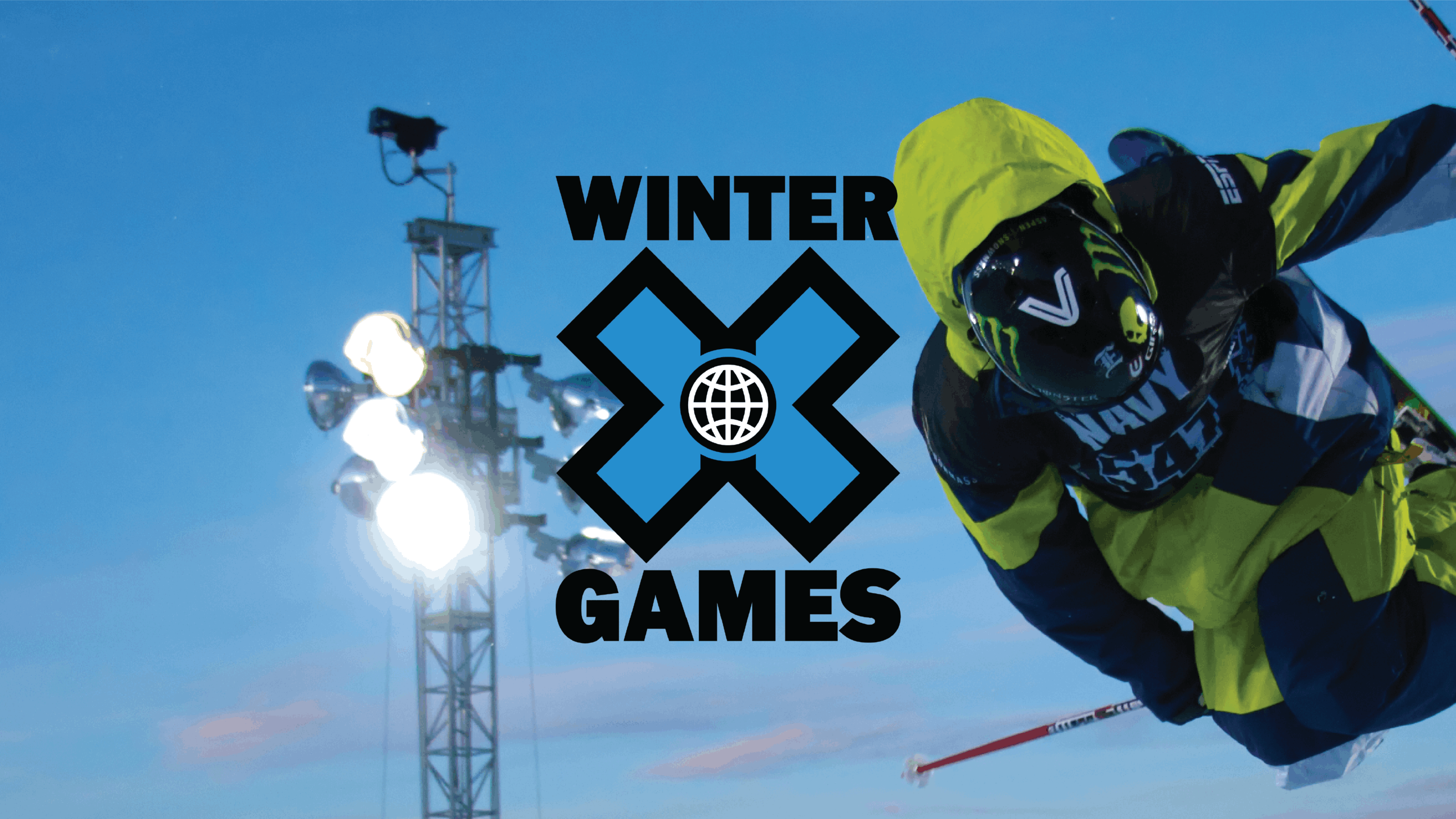 A skier in green jumps and crosses their skis. Behind them is a stadium light. The Winter X Games logo is laid on top.