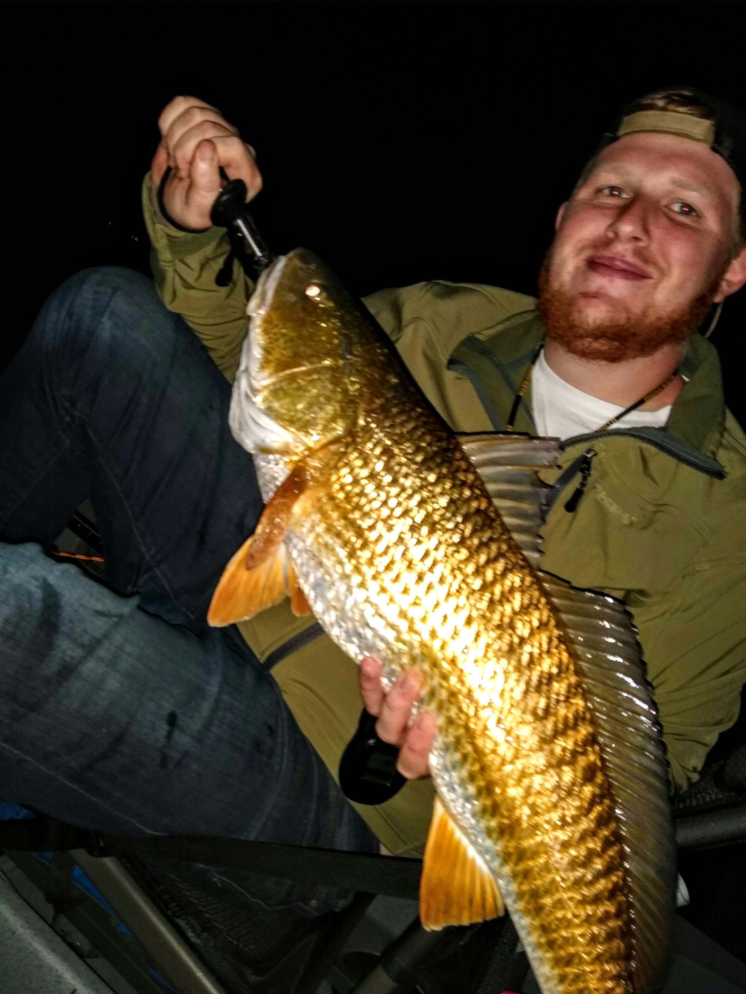 The author holds up a large redfish at night. The photo is taken with flash which reflects off the fish's scales. 