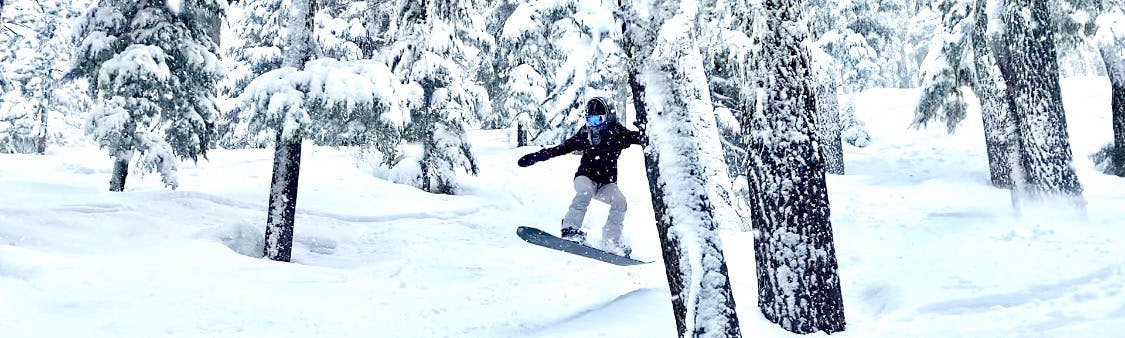 A woman snowboarding through the trees.