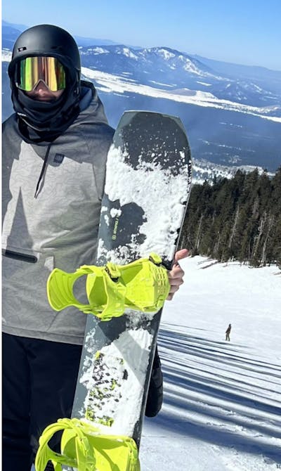 A man on a ski run holding a Ride Mtnpig Snowboard.
