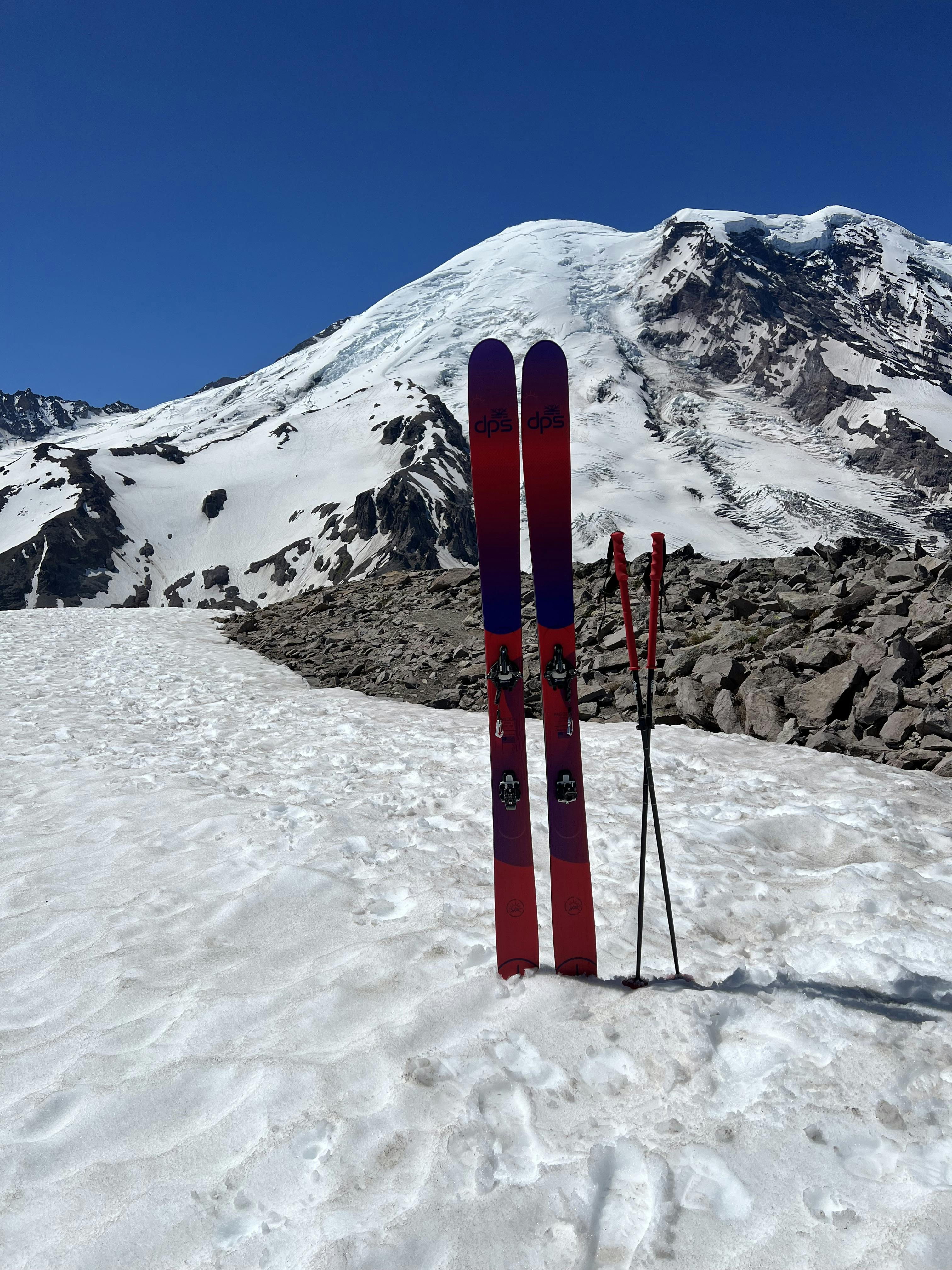 The DPS Pagoda Tour 100 RP Dreamtime Skis · 2021 sticking in the snow with a snowy mountain in the background. 