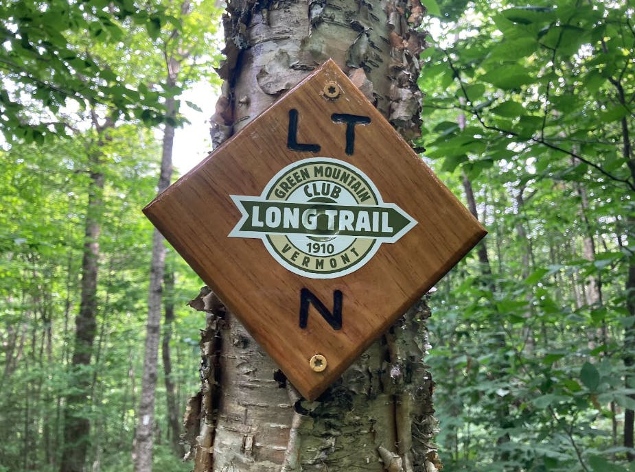 A wooden sign nailed into a tree that reads "LT N. Green Mountain Long Trail Club Vermont."